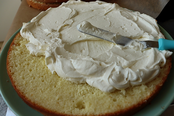 Sponge cake layer being covered with mascarpone cream with a spatula