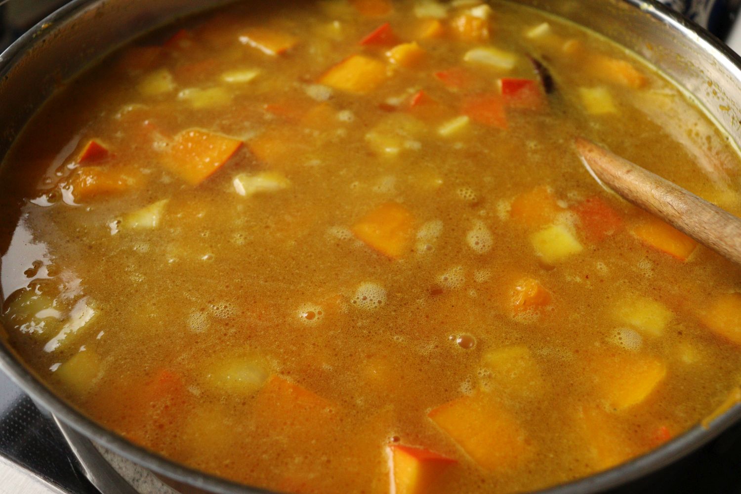 Boiled pumpkin, celery root, carrots, potatoes and onion cubes in a pan for making pumpkin soup