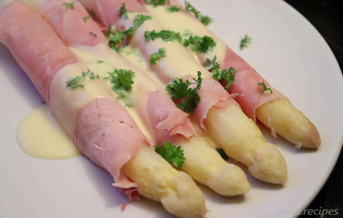 White Asparagus served with ham and topped with hollandaise sauce and fresh parsley leaves