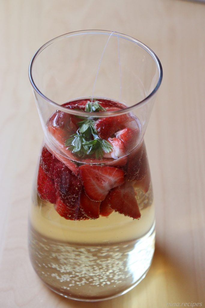 Maibowle (German May Wine) in a glass, with fresh strawberries and waldmeister (sweet woodruff)