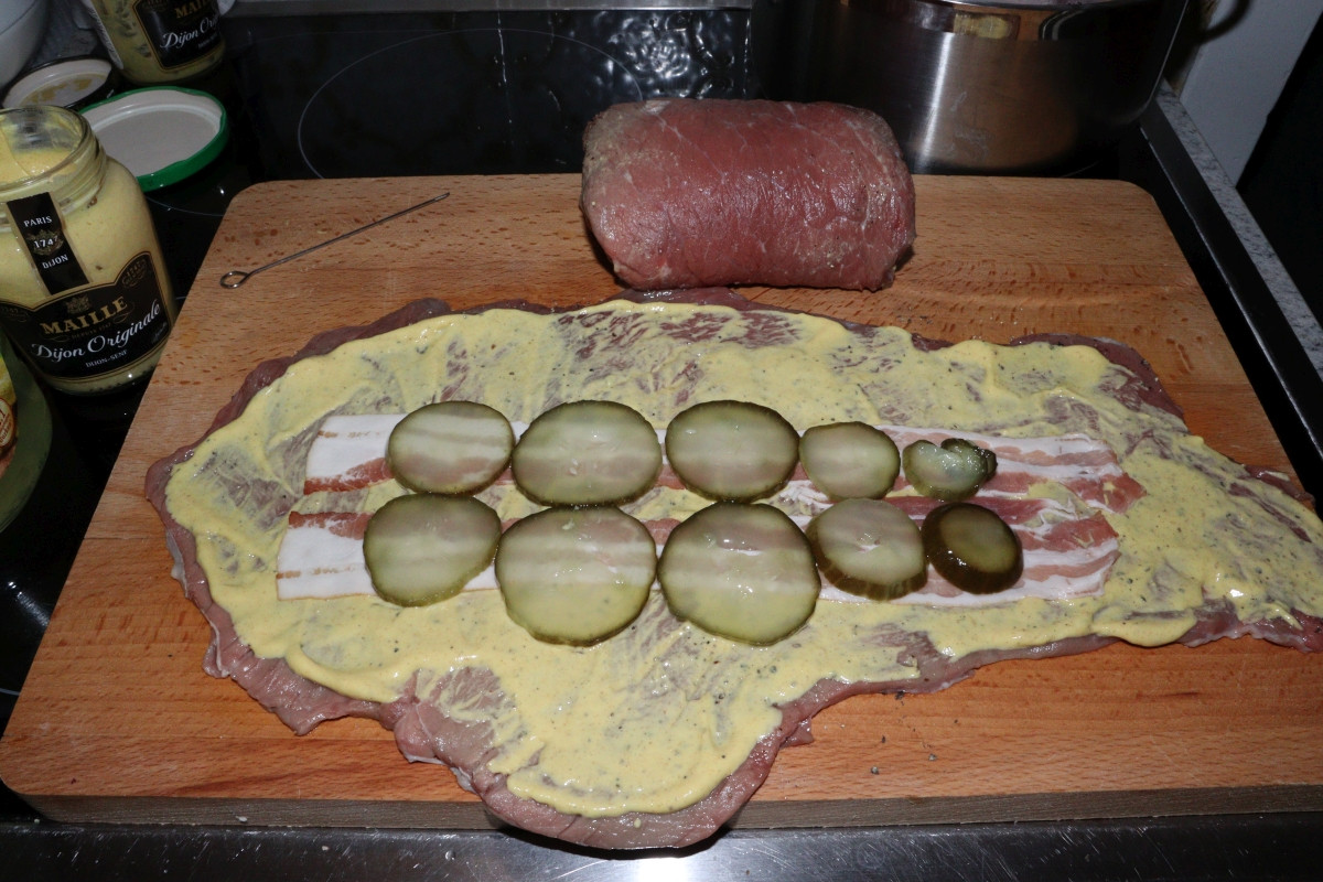 Beef slice covered in mustard, with bacon stripes and pickled cucumbers, for Rinderrouladen