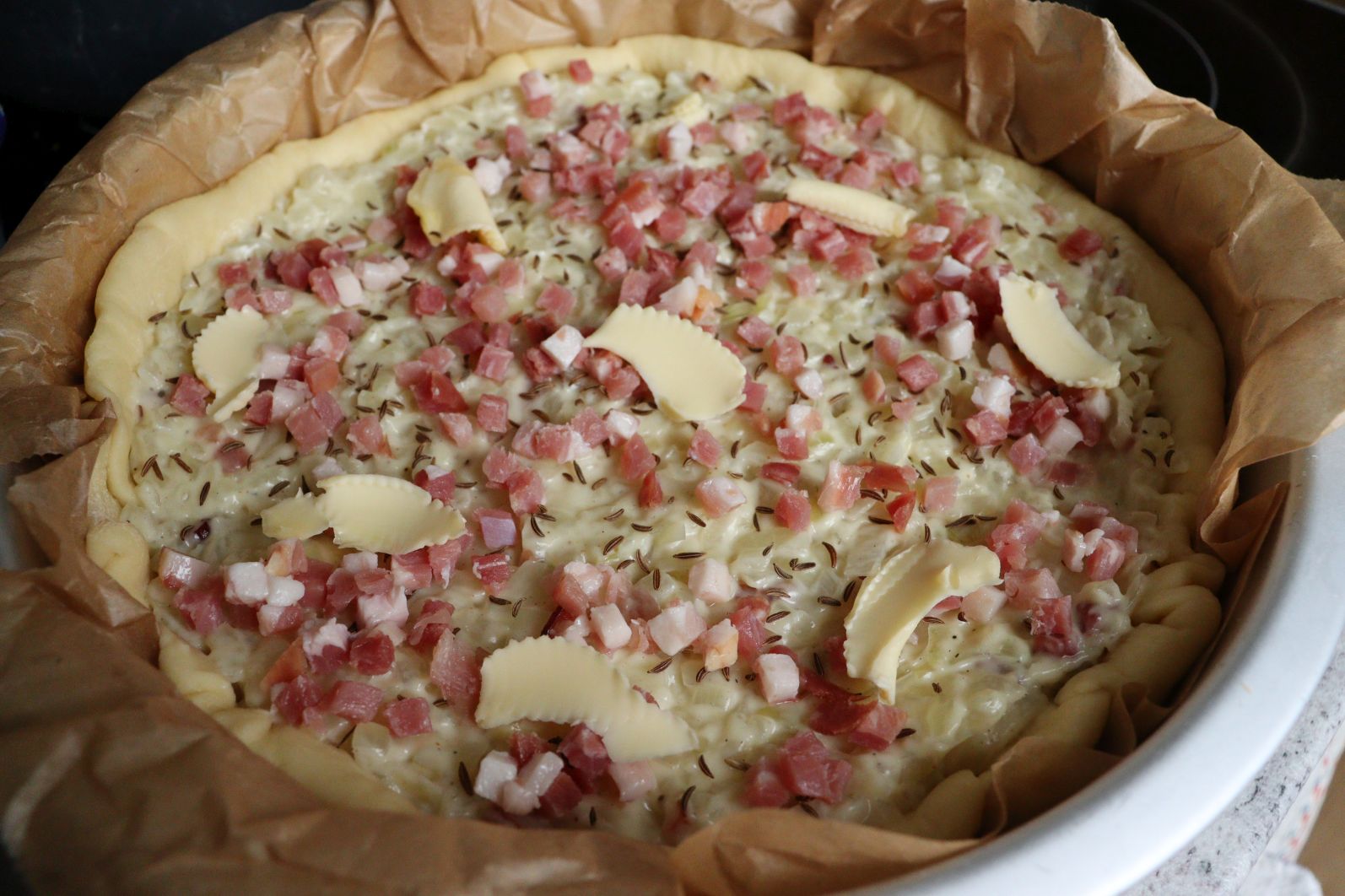 Raw Zwiebelkuchen - Onion Pie with onion and bacon filling, caraway seeds, bacon pieces and butter flakes on top