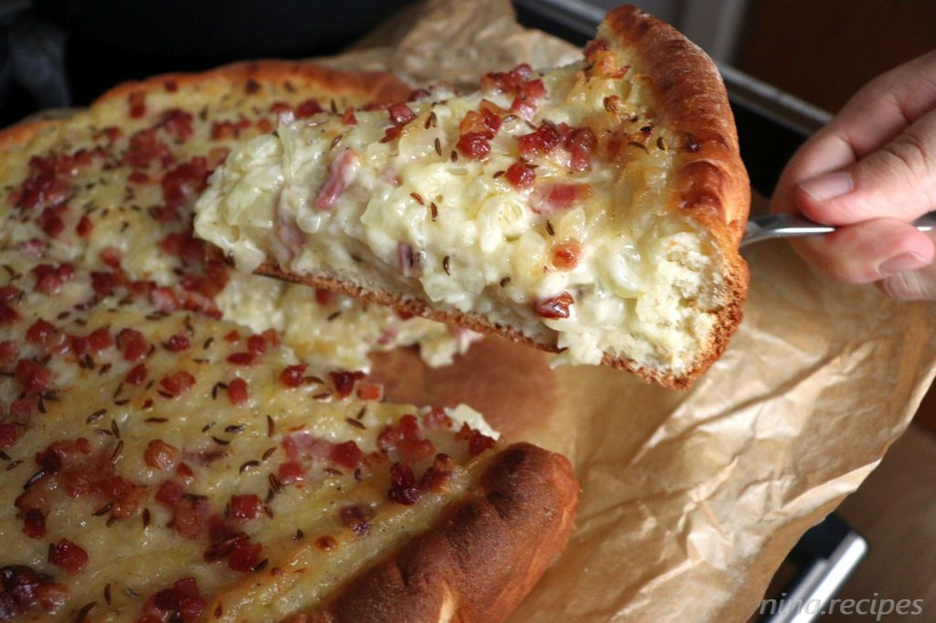 Holding a piece of Zwiebelkuchen - Onion Pie next to the full pie